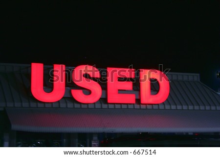 sign in front of used car lot at night.