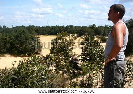 man standing on will looking around the sand pit where he goes 4 wheeling with friends