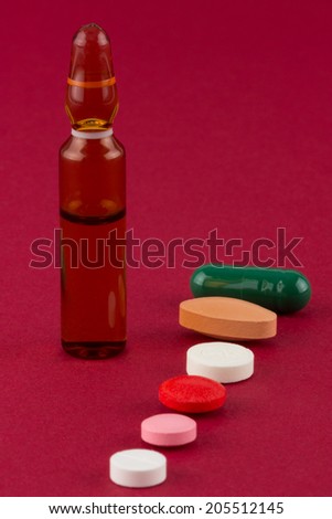 Multiple colored and shaped pills and ampoule on red background