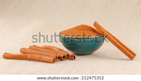 Ground cinnamon powder in green porcelain bowl and cinnamon sticks on rustic table cloth
