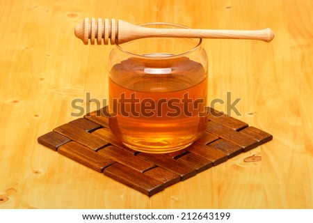 Honey in glass jar with wooden dipper on wooden tabletop and mat