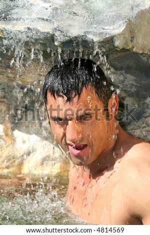 Handsome male model posing underneath a waterfall