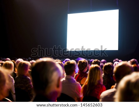 Crowd audience in dark looking at bright screen