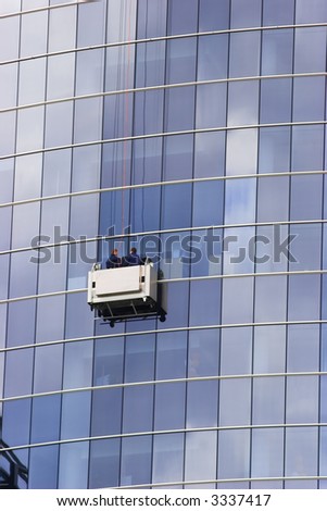 Two window cleaners in a gondola cleaning the windows of a corporate office skyscraper.