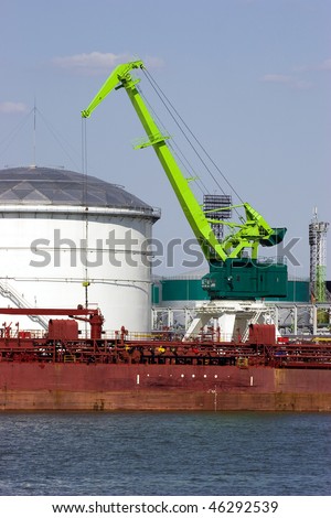 Green port crane working. White cylindrical tanks for industrial chemicals and petroleum products in background