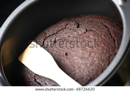 Chocolate cake in a round baking tin with spatula
