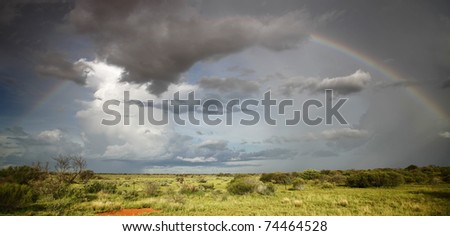 Full rainbow arcing over Western Australian outback landscape.