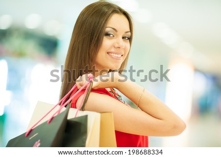 Beautiful smiling girl in a red dress with long hair shopping, holding shopping bags