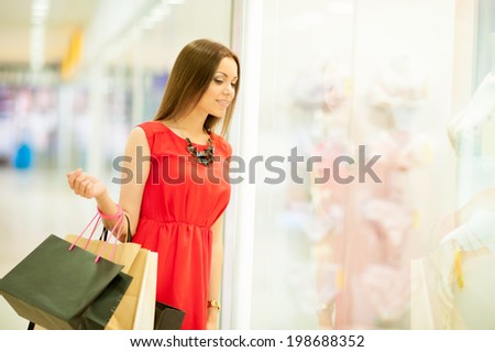 Beautiful smiling girl in a red dress with long hair shopping, holding shopping bags