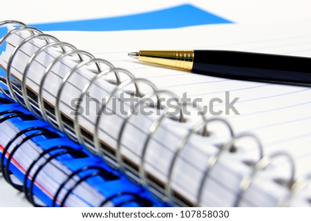 Close up of a pen resting on a lined, coil notebook