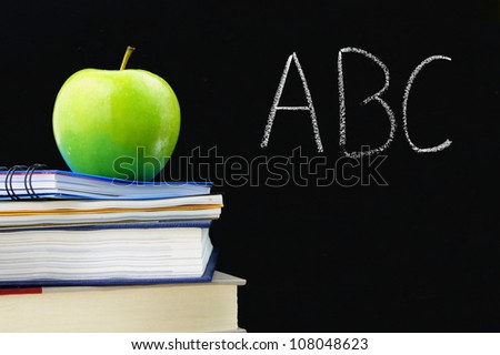 ABC written on a blackboard with books and apple in front