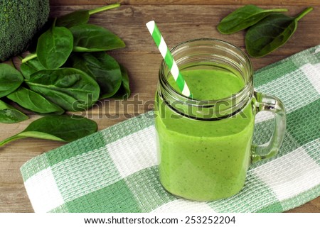 Healthy green smoothie with spinach in a jar mug with checkered cloth against wood