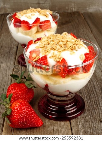 Strawberry and banana yogurt parfaits with granola on rustic wood background