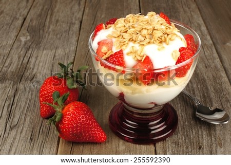 Strawberry and banana yogurt parfait with granola on rustic wood background