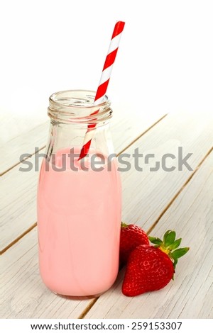 Strawberry milk in traditional bottle with straw on white wood table