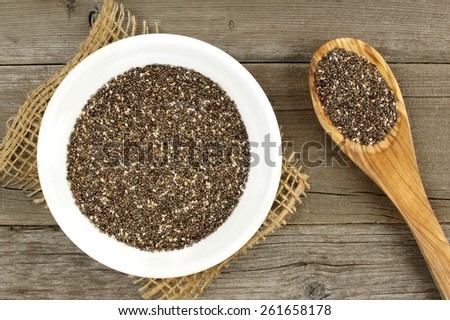 Bowl and spoon filled with chia seeds over a wood background