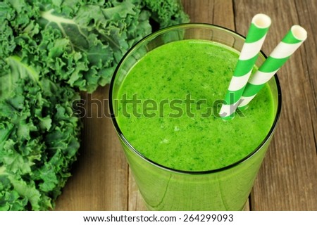 Healthy green kale smoothie in a glass with straws on wood background. Close up, above view