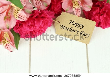 Border of pink carnation and lily flowers with Happy Mother\'s Day gift tag on white wood background