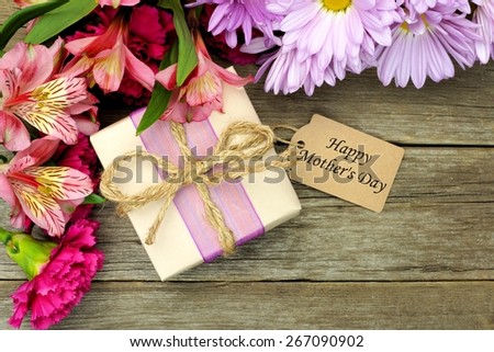 Border of flowers with Mother\'s Day gift box and tag against a rustic wood background