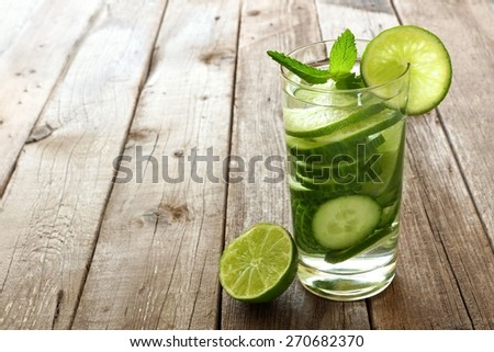 Nutritious detox water with lime and cucumber in a glass against a wood background