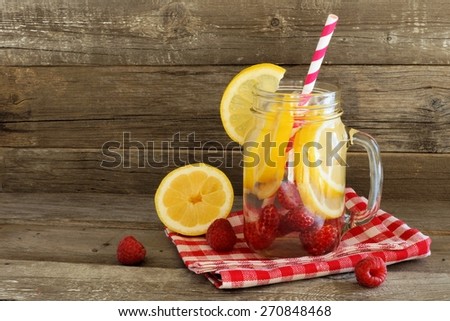 Detox water with lemon and raspberries in a jar with straw and cloth against a wood background
