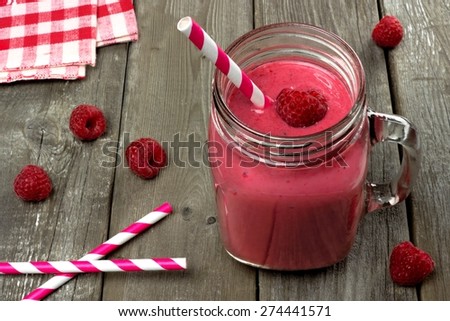 Pink raspberry smoothie in a mason jar with straws on a rustic wood background