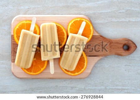 Frozen orange flavored yogurt pops with fruit slices on a wooden paddle board