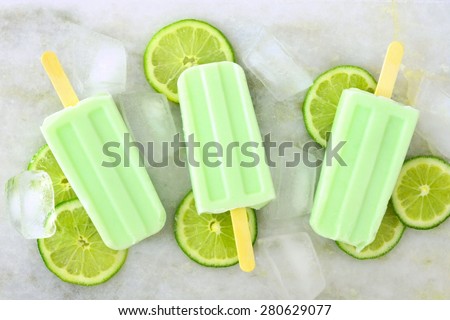 Healthy lime yogurt popsicles with fresh lime slices scattered on a white marble background