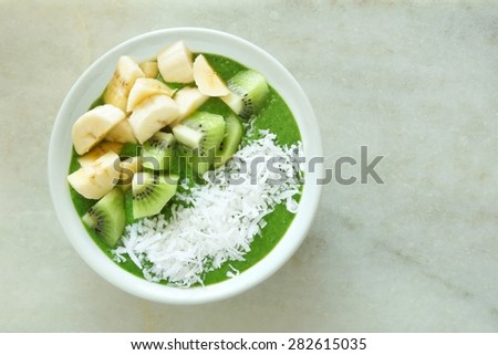 Green smoothie bowl with bananas, fresh kiwi and shredded coconut on a white marble background