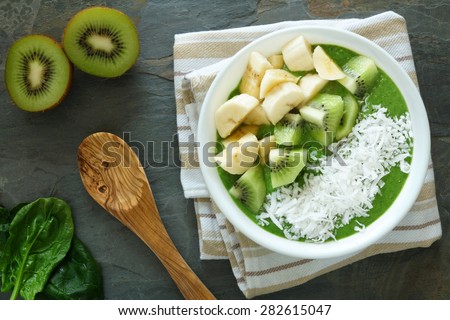 Green smoothie bowl with spinach,fresh kiwi fruit, bananas and coconut on a slate background