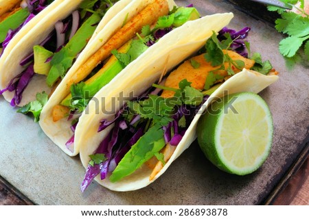 Spicy fish tacos with red cabbage slaw, avocado and lime juice on vintage tray