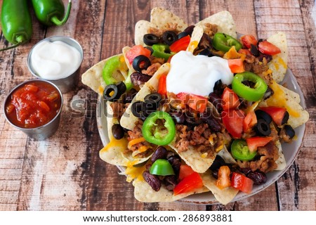 Plate of Mexican nacho chips topped with sour cream, ground meat, jalapenos, tomatoes, beans and melted cheese