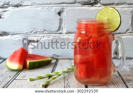 Watermelon lime water in a mason jar glass with melon slices and straws against white rustic wood and bricks