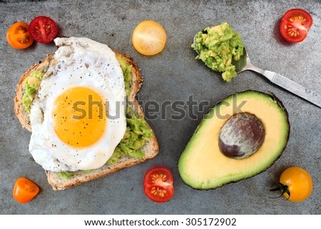 Open avocado, egg sandwich on whole grain bread with cherry tomatoes on rustic baking tray