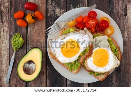 Healthy avocado, egg open sandwiches on a plate with cherry tomatoes on a rustic wood background