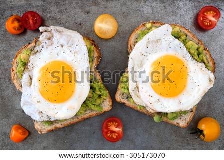 Open avocado, egg sandwiches on whole grain bread with tri-colored tomatoes on rustic baking tray