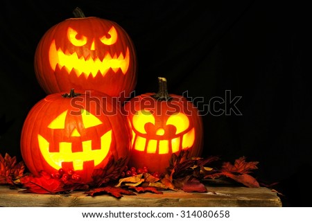 Stacked Halloween Jack o Lanterns illuminated at night with old wood and autumn leaves