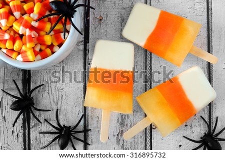 Halloween candy corn popsicles downward view on old white wood background with toy spiders