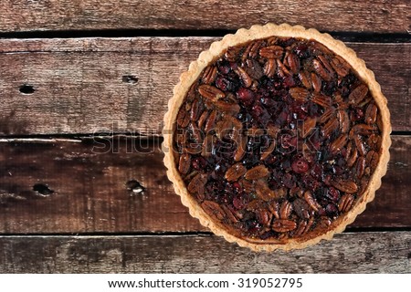 Pecan and cranberry autumn pie on rustic old wood, overhead view