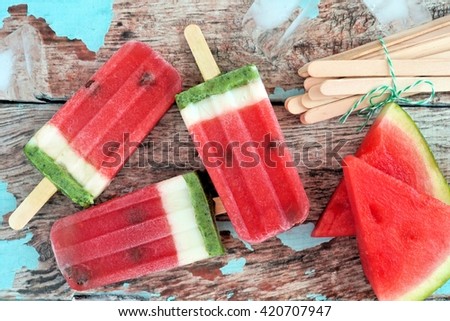 Homemade watermelon ice pops with melon slices against rustic wood background