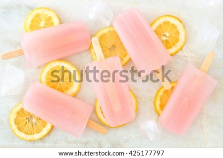 Group of pink lemonade popsicles with lemon slices, ice cubes on a white marble background