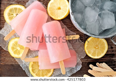 Pink lemonade popsicles with ice pail and lemon slices on a rustic wood background