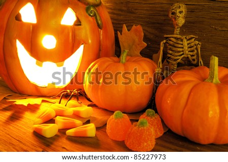 Halloween night scene closeup with glowing jack-o-lantern, pumpkins, candy and skeleton