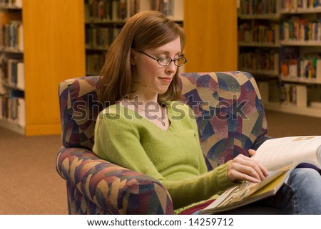 a young woman sitting in a chair at the library reading a magazine