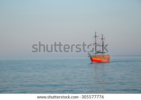 red sailboat sailing ship in the ocean gradually and proudly in the distant sky