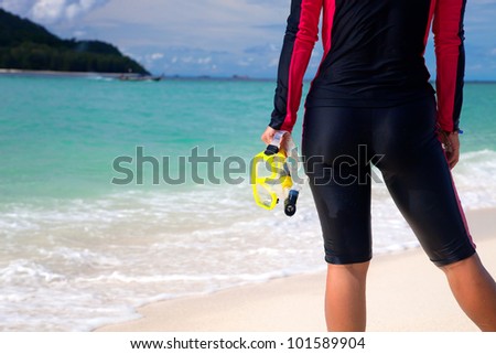 Woman in diving suite hold mask in her hand by the blue sea
