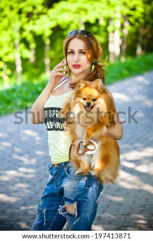 Beautiful girl talking on a cell phone with a dog in her arms
