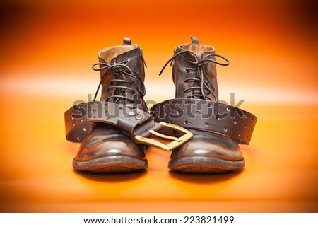 Autumn still life: men\'s leather shoes and a leather belt with a buckle. Fashion boots and belt of brown color on a red background