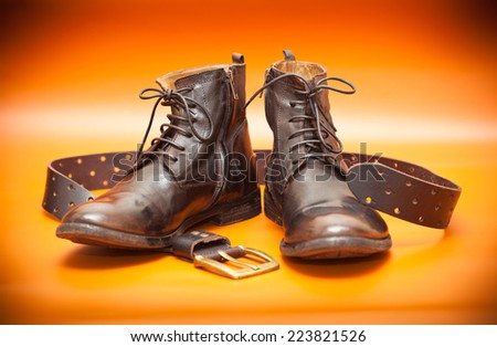 Autumn still life: men\'s leather shoes and a leather belt with a buckle. Fashionable shoes and brown belt on an orange background