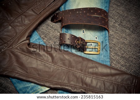 Blue jeans, a leather belt with a buckle and leather jacket. dark tone